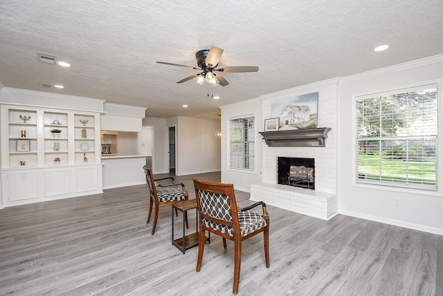 dining area with a fireplace, ceiling fan, light wood-type flooring, and a textured ceiling