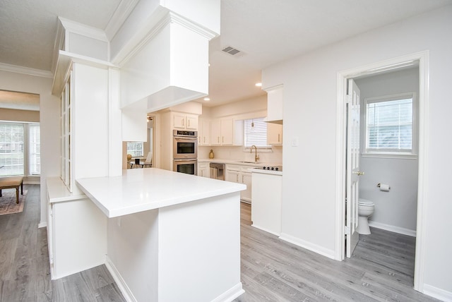 kitchen with double oven, kitchen peninsula, white cabinetry, and a healthy amount of sunlight