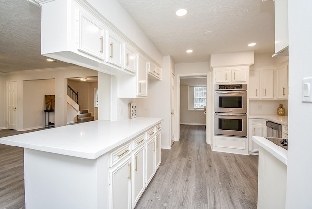 kitchen featuring kitchen peninsula, light wood-type flooring, a textured ceiling, stainless steel appliances, and white cabinetry