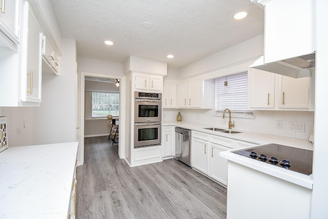 kitchen with white cabinets, sink, light wood-type flooring, a textured ceiling, and appliances with stainless steel finishes