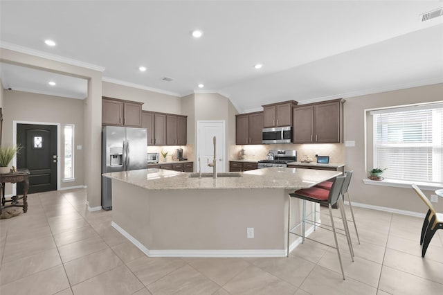 kitchen featuring sink, appliances with stainless steel finishes, backsplash, light stone counters, and an island with sink