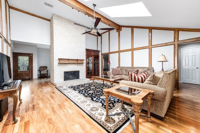 living room with a skylight, ceiling fan, beamed ceiling, light hardwood / wood-style floors, and a fireplace