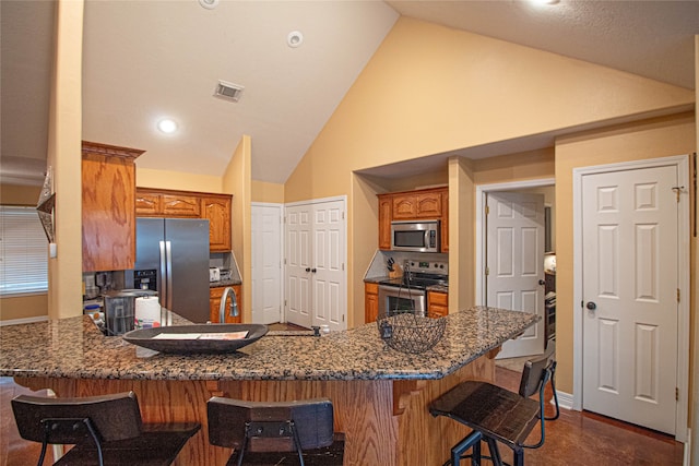 kitchen with kitchen peninsula, appliances with stainless steel finishes, high vaulted ceiling, dark stone countertops, and a breakfast bar area