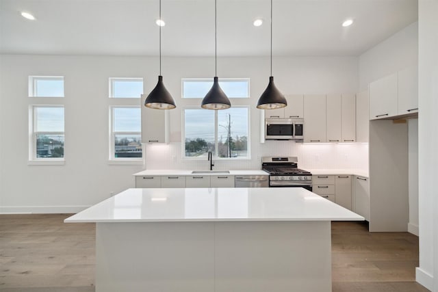 kitchen featuring white cabinets, stainless steel appliances, decorative light fixtures, and a kitchen island