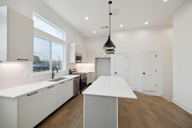 kitchen with pendant lighting, a center island, stainless steel appliances, white cabinetry, and sink