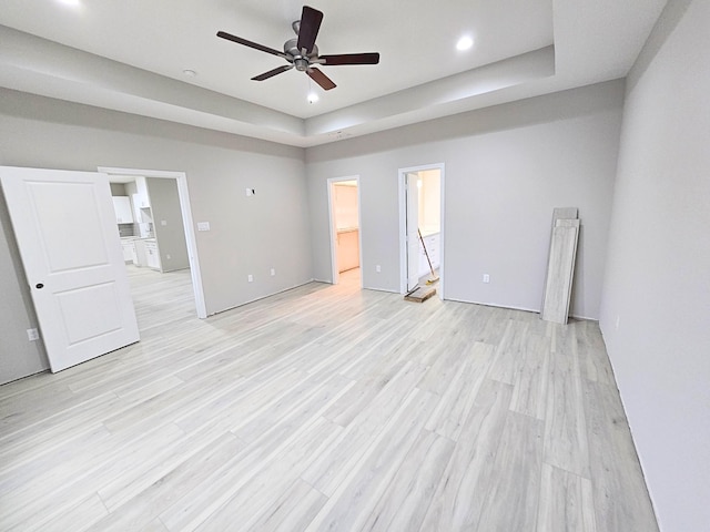 unfurnished bedroom with a walk in closet, ceiling fan, light wood-type flooring, a tray ceiling, and a closet