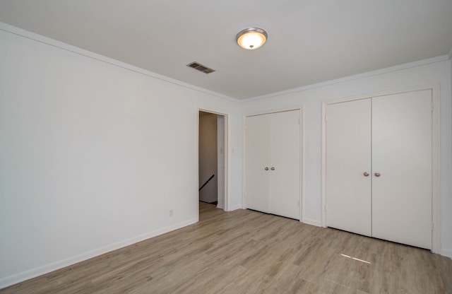 unfurnished bedroom with multiple closets, crown molding, and light hardwood / wood-style flooring