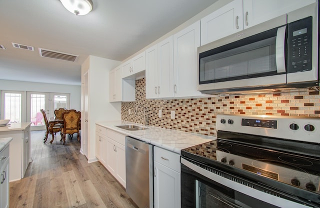 kitchen featuring white cabinetry, sink, light hardwood / wood-style floors, decorative backsplash, and appliances with stainless steel finishes