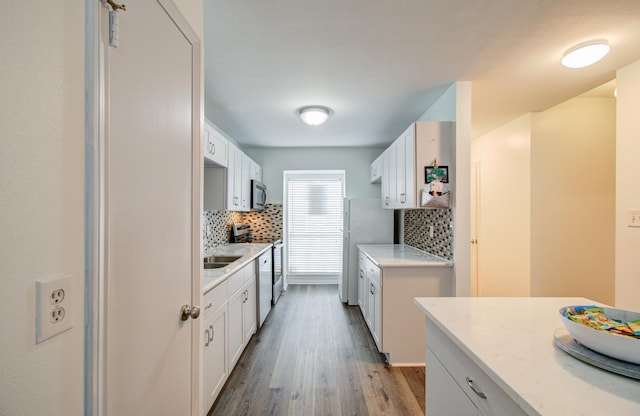 kitchen with decorative backsplash, stainless steel appliances, white cabinetry, and light hardwood / wood-style floors