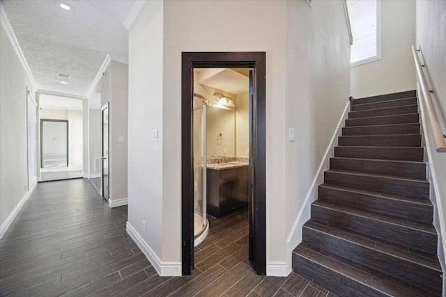 stairs featuring crown molding, wood finish floors, a textured ceiling, and baseboards