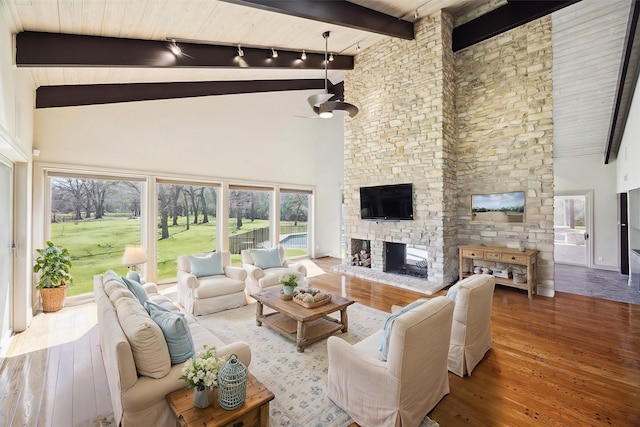 living area featuring high vaulted ceiling, beamed ceiling, a stone fireplace, and hardwood / wood-style floors