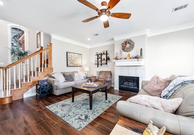 living room featuring ceiling fan, ornamental molding, a textured ceiling, and a tile fireplace