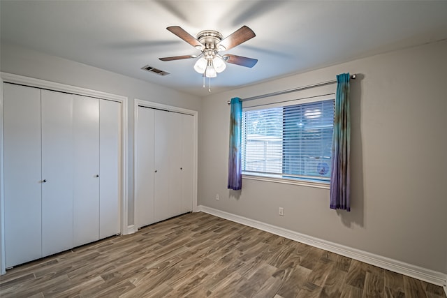 unfurnished bedroom with ceiling fan, wood-type flooring, and two closets