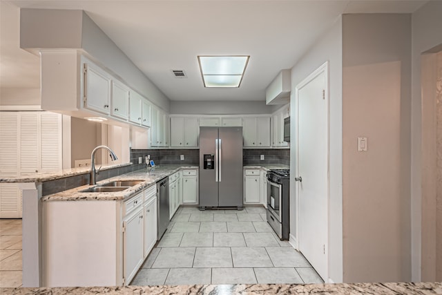 kitchen featuring kitchen peninsula, decorative backsplash, light stone counters, stainless steel appliances, and sink