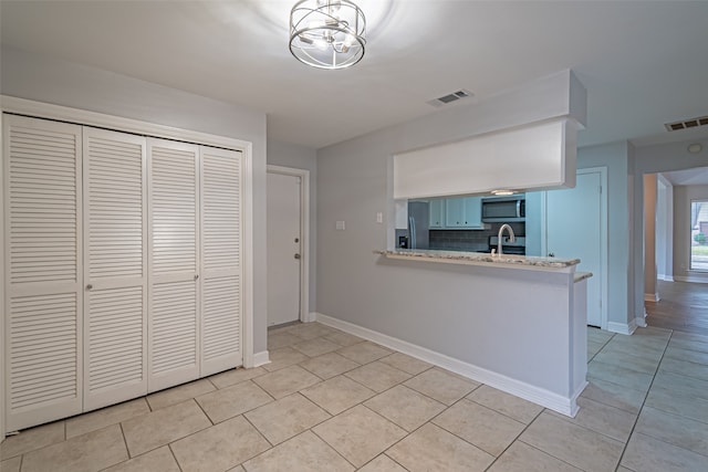 kitchen featuring kitchen peninsula, appliances with stainless steel finishes, tasteful backsplash, light tile patterned floors, and a notable chandelier