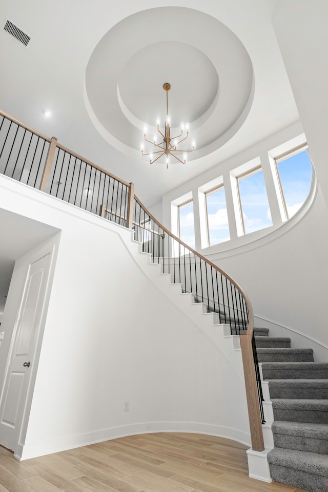 stairs featuring a tray ceiling, a chandelier, and wood-type flooring