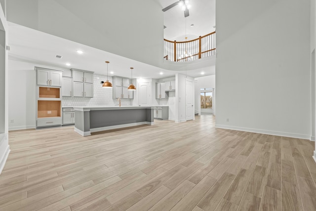 unfurnished living room with ceiling fan, light hardwood / wood-style flooring, a high ceiling, and sink