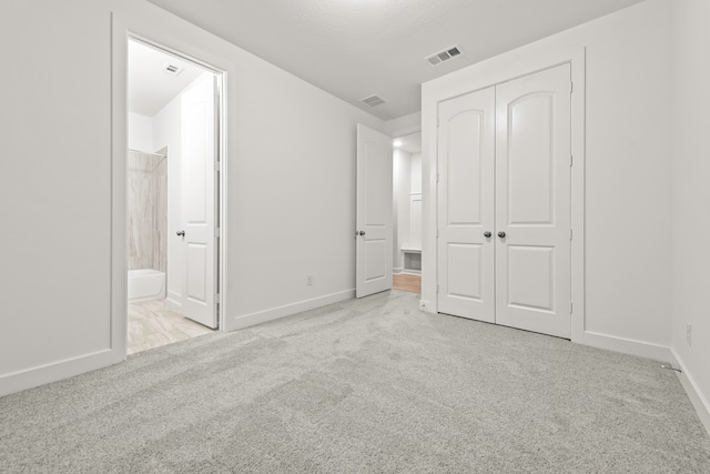 unfurnished bedroom with a closet, light carpet, and ensuite bath