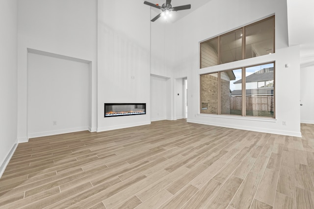 unfurnished living room featuring ceiling fan, light wood-type flooring, and a high ceiling