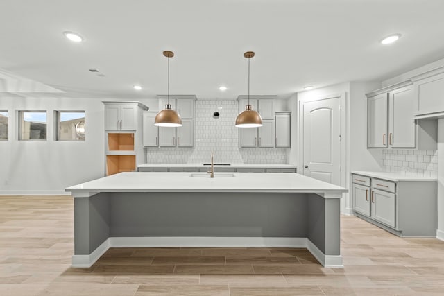 kitchen featuring a center island with sink, decorative backsplash, gray cabinetry, and sink