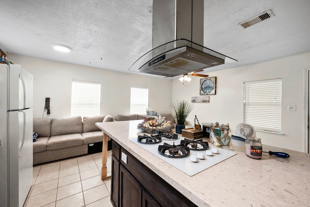 kitchen featuring a textured ceiling, white appliances, island range hood, dark brown cabinets, and light tile patterned floors