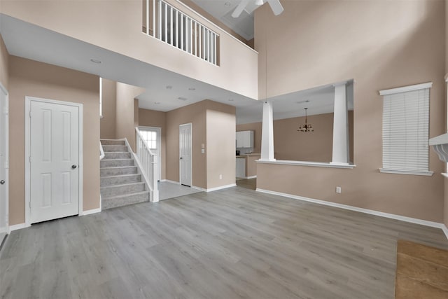 unfurnished living room with light hardwood / wood-style flooring, ceiling fan with notable chandelier, and a high ceiling