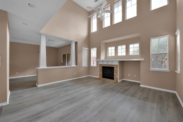 unfurnished living room featuring a high ceiling, hardwood / wood-style flooring, a stone fireplace, and ceiling fan