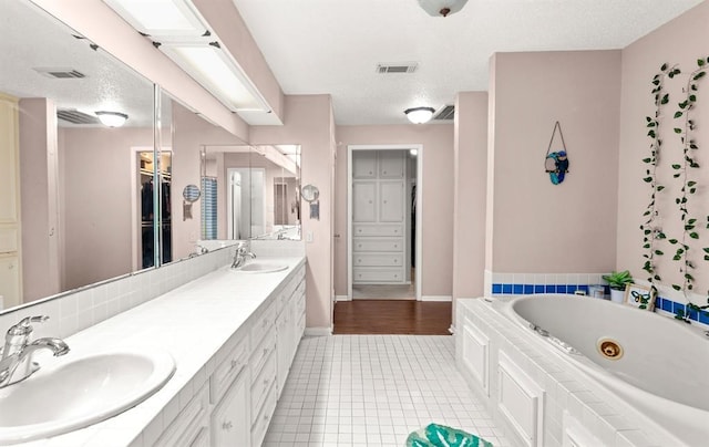 bathroom featuring tile patterned flooring, vanity, a tub to relax in, and a textured ceiling