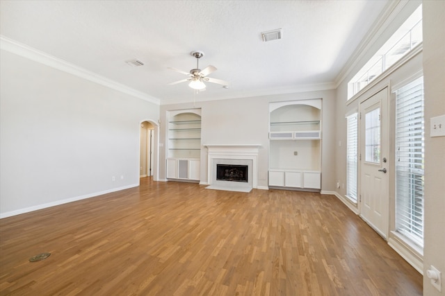 unfurnished living room with wood-type flooring, built in features, ceiling fan, and crown molding