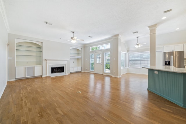 unfurnished living room with ceiling fan, built in features, crown molding, and light wood-type flooring