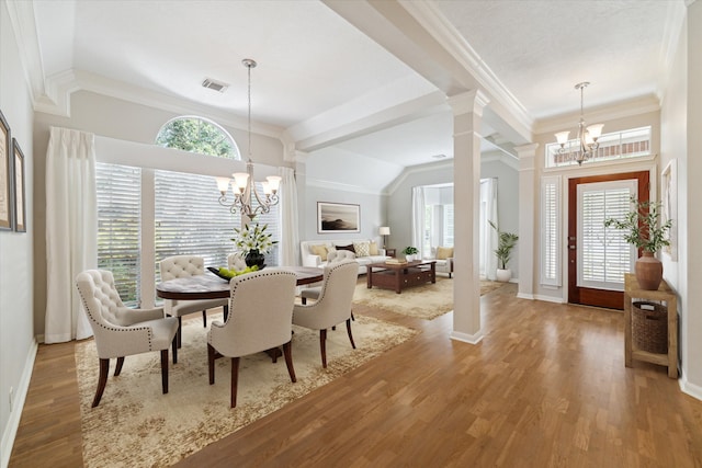 dining space with wood-type flooring, decorative columns, an inviting chandelier, and crown molding