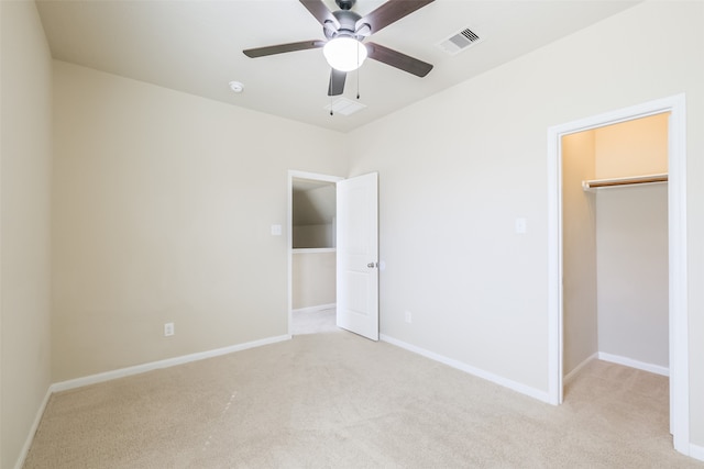 unfurnished bedroom with a closet, a walk in closet, light colored carpet, and ceiling fan