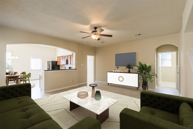 living room featuring ceiling fan with notable chandelier and light hardwood / wood-style flooring