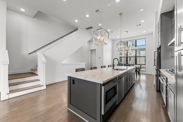 kitchen featuring stainless steel appliances, light stone counters, dark hardwood / wood-style floors, decorative light fixtures, and a kitchen island with sink