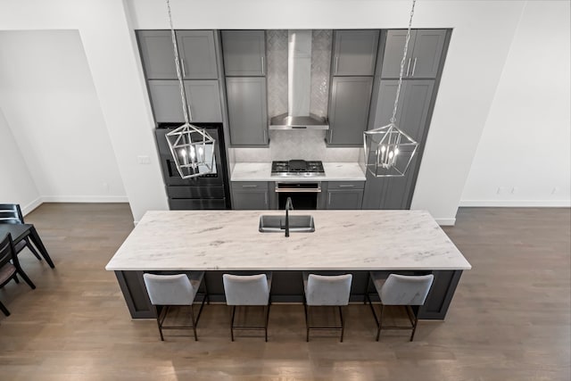 kitchen featuring gray cabinetry, a kitchen bar, wall chimney range hood, and appliances with stainless steel finishes