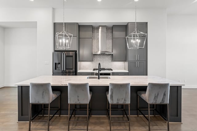 kitchen featuring light stone counters, gray cabinetry, stainless steel appliances, a spacious island, and wall chimney range hood