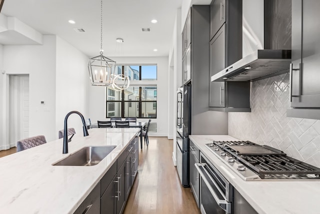 kitchen with pendant lighting, wall chimney range hood, sink, hardwood / wood-style flooring, and stainless steel appliances