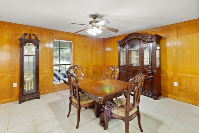 dining room with ceiling fan, wood walls, and light tile patterned flooring