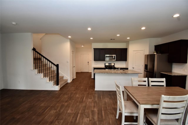 kitchen with an island with sink, dark wood-type flooring, appliances with stainless steel finishes, and light stone countertops