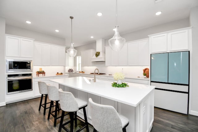 kitchen featuring built in appliances, a center island with sink, white cabinetry, and premium range hood