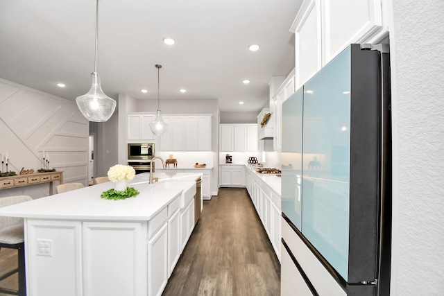 kitchen with a kitchen island with sink, dark wood-type flooring, hanging light fixtures, white cabinetry, and stainless steel appliances