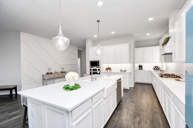 kitchen featuring stainless steel appliances, dark wood-type flooring, an island with sink, pendant lighting, and white cabinets