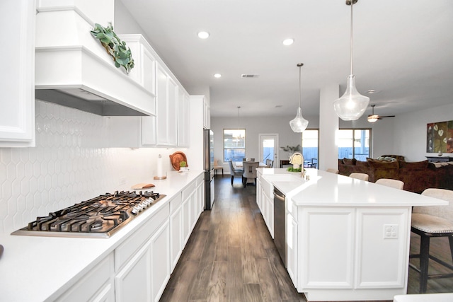 kitchen with a kitchen bar, appliances with stainless steel finishes, dark wood-type flooring, decorative light fixtures, and an island with sink