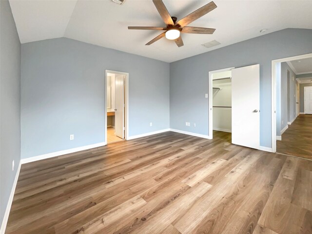 unfurnished bedroom with a spacious closet, ceiling fan, ensuite bathroom, a closet, and hardwood / wood-style flooring