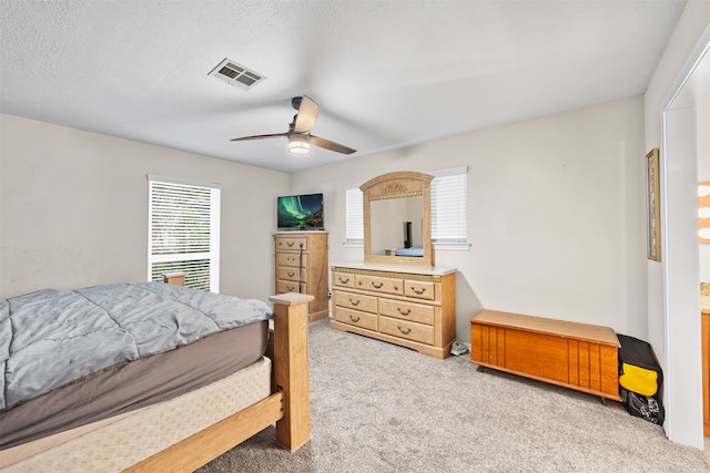 bedroom featuring ceiling fan, light colored carpet, and a textured ceiling