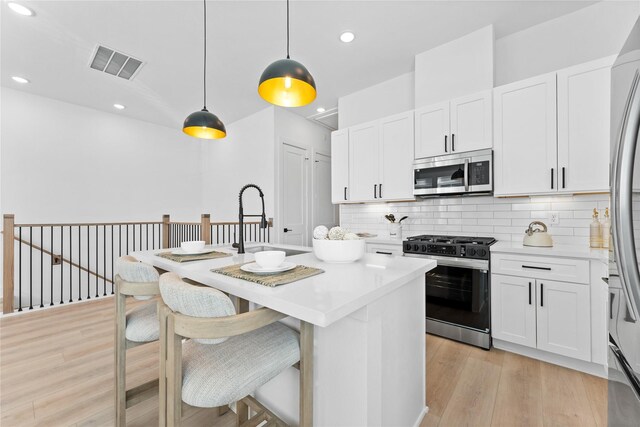 3109 Jensen Dr Unit B, Houston, TX 77026 - kitchen with light wood-type flooring, stainless steel appliances, pendant lighting, white cabinets, and an island with sink