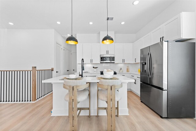 3109 Jensen Dr Unit B, Houston, TX 77026 - kitchen with stainless steel appliances, decorative light fixtures, white cabinets, light hardwood / wood-style floors, and an island with sink