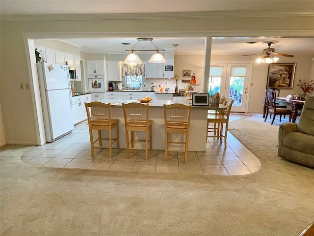 kitchen with light carpet, white appliances, white cabinetry, hanging light fixtures, and a breakfast bar area