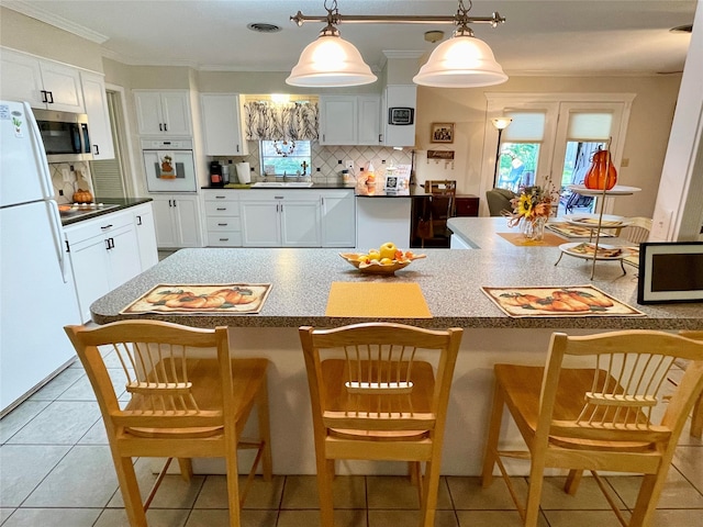 kitchen featuring white cabinets, pendant lighting, white appliances, and a kitchen bar