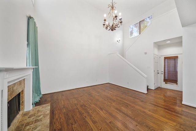 unfurnished living room featuring a notable chandelier, dark wood-type flooring, high vaulted ceiling, and a tiled fireplace